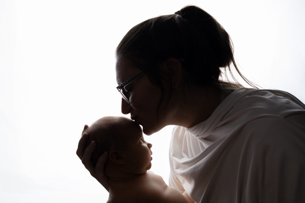 Mom and newborn silhouette done in Minot, ND. Mom is kissing her babys' head while the little one is looking up at her mom.