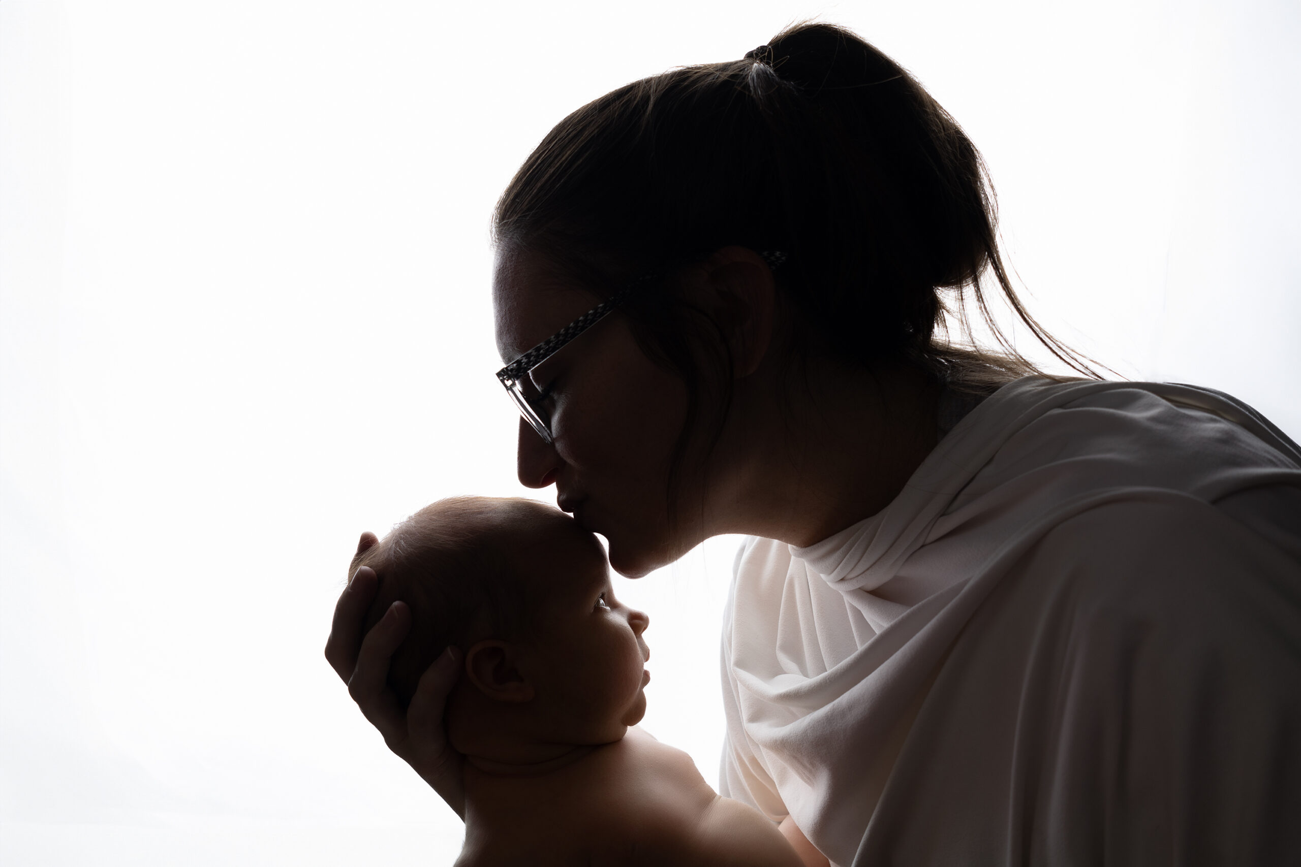 Mom and newborn silhouette done in Minot, ND. Mom is kissing her newborns head while the newborn has their eyes closed.