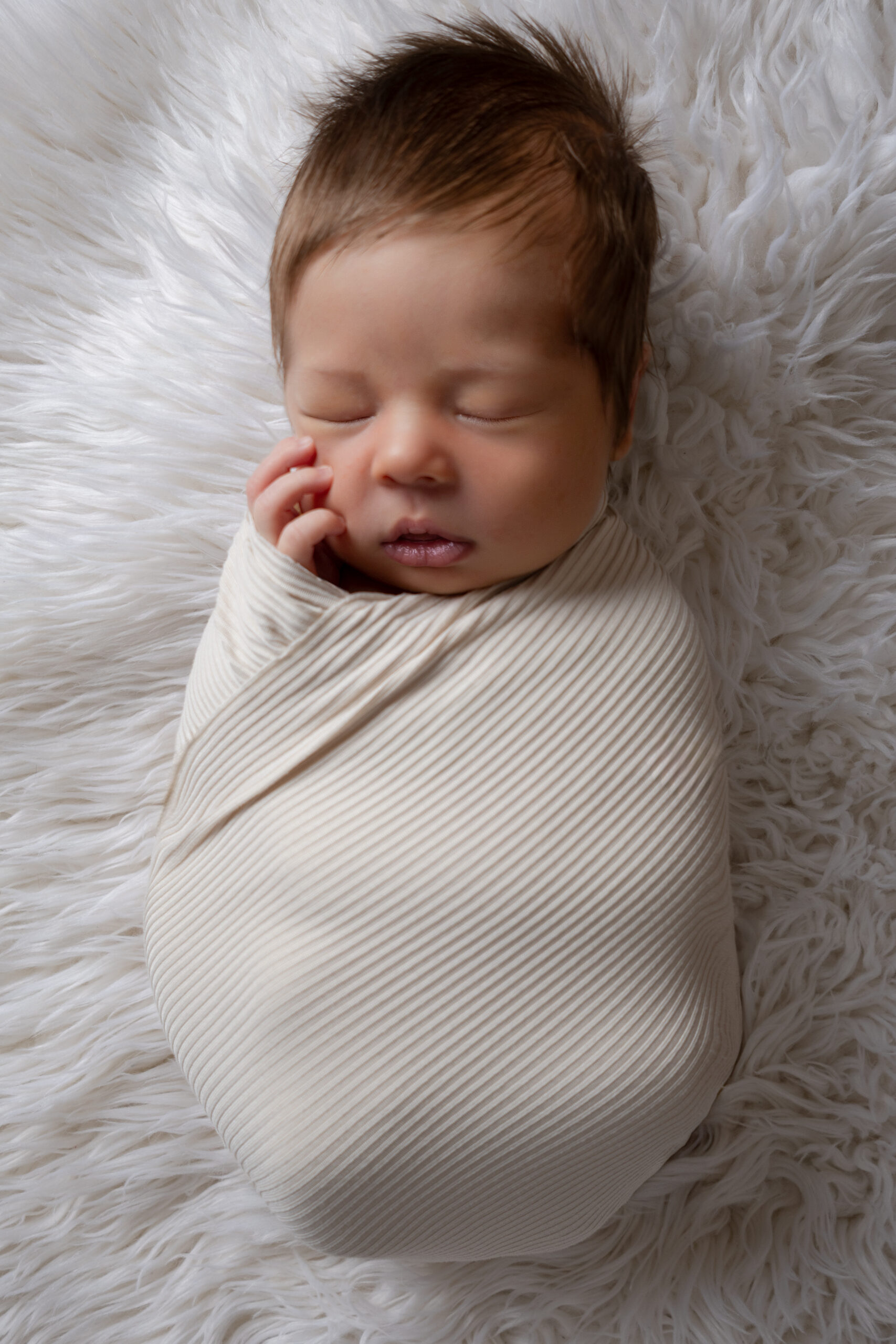 Wrapped Newborn with hand against cheek.